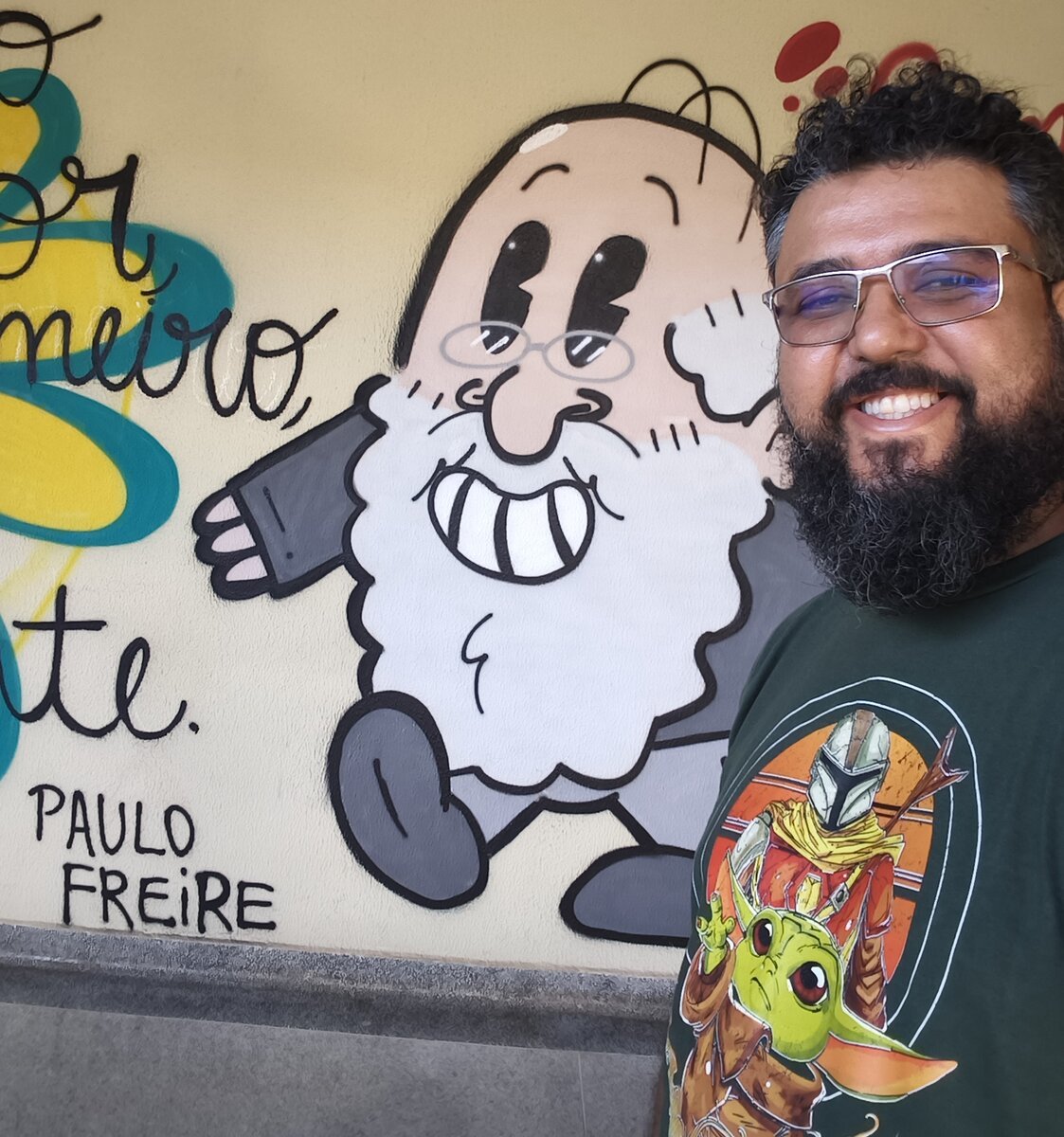 Tio Rafa em frente a um mural com a frase de Paulo Freire
